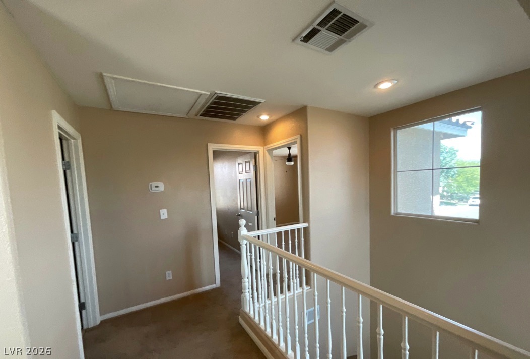 10841 Paradise Road Henderson, NV 89052 - Photo 17 of 35 A warm, neutral-toned hallway with carpeted flooring and white railings leading to various rooms.
