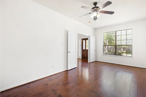 an empty room with wooden floor chandelier fan and windows