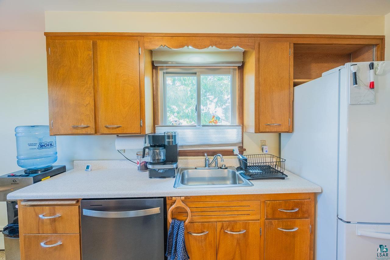 101 2nd Avenue North Biwabik, MN 55708 - Photo 7 of 44 Kitchen workspace featuring wood cabinetry, light-toned countertops, a stainless steel sink, a stainless steel dishwasher, and a window with natural light