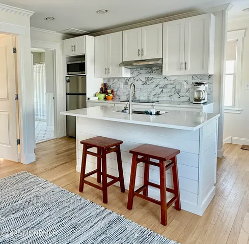 a kitchen with stainless steel appliances granite countertop a stove a sink a refrigerator and white cabinets with wooden floor