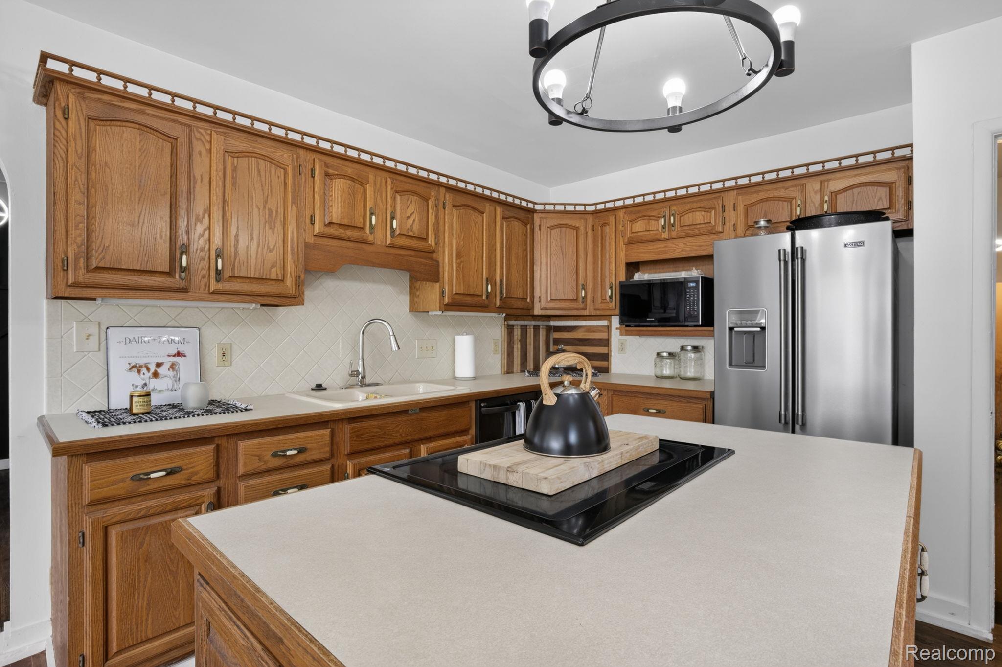 1209 Beatrice Street Flushing, MI 48433 - Photo 8 of 39 Kitchen featuring light countertops, black appliances, wood finish cabinets, decorative backsplash, and a center island
