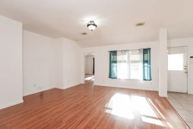 a view of an empty room with wooden floor and a window