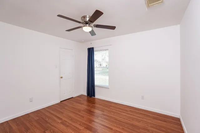 an empty room with wooden floor fan and windows