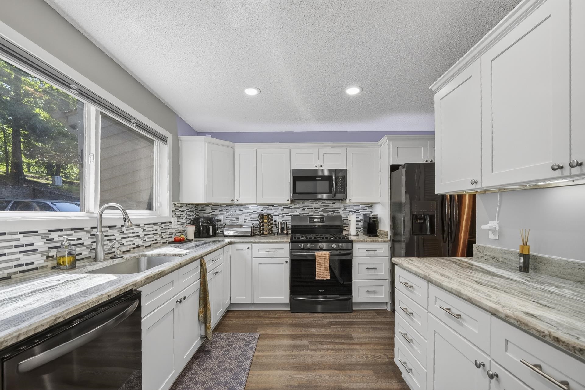 74 Driftwood Road Counce, TN 38326 - Photo 6 of 40 Kitchen featuring white shaker-style cabinetry, stainless steel appliances, mosaic tile backsplash, wood-finish flooring, and light-toned granite countertops