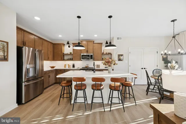 a kitchen with stainless steel appliances kitchen island granite countertop a dining table chairs and a refrigerator