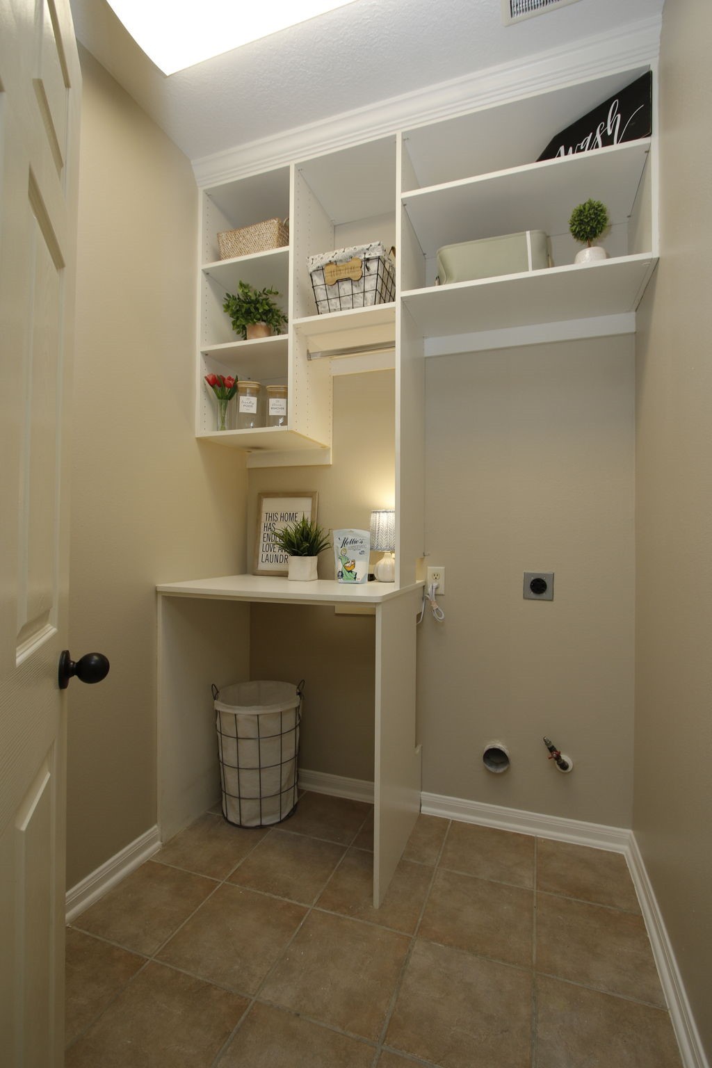 9203 Memorial Pines Way Spring, TX 77379 - Photo 35 of 45 This photo showcases a compact laundry room with beige walls and tile flooring. It features built-in shelving for storage, a countertop for folding, and hookups for a washer and dryer.