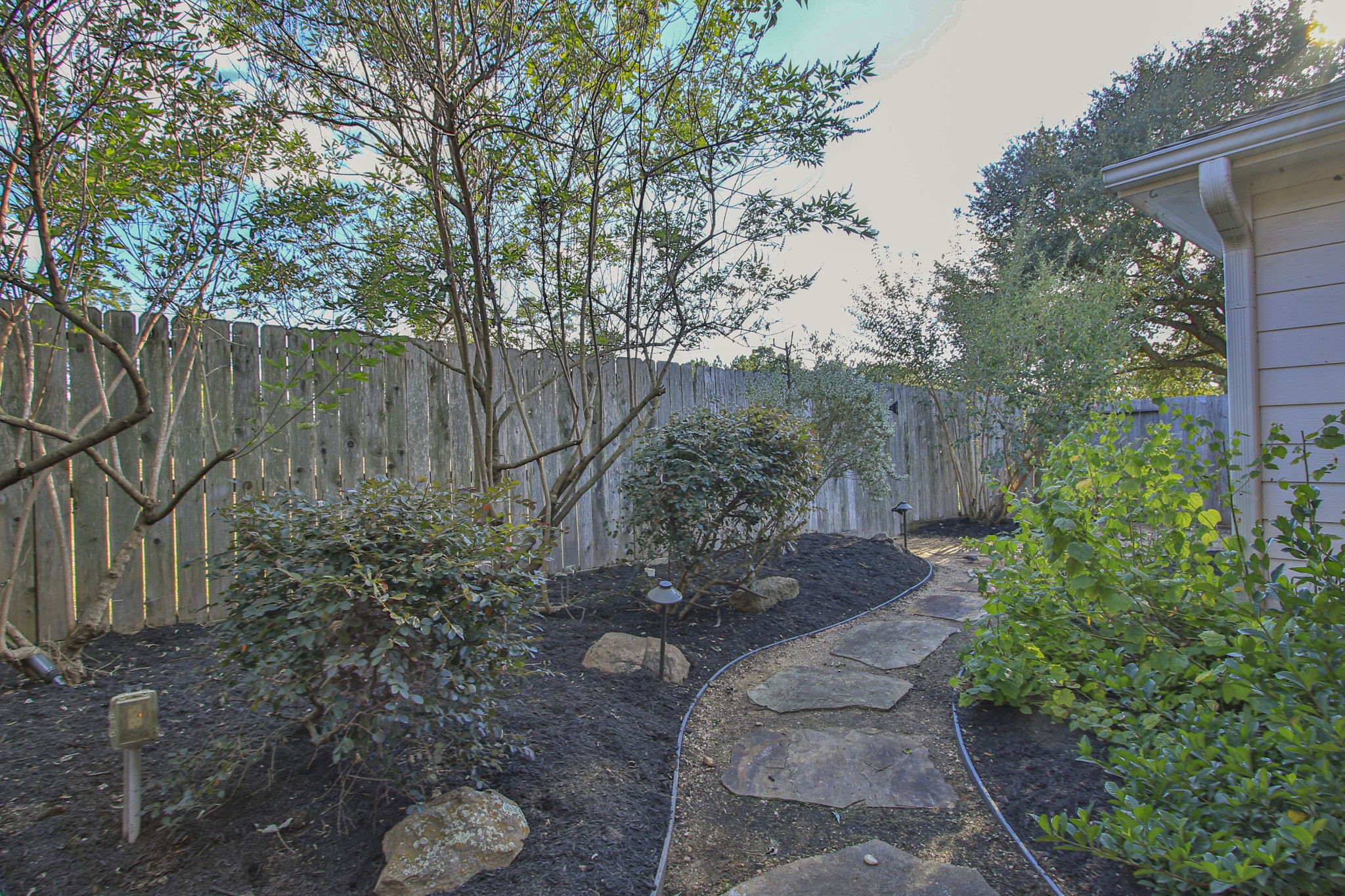 9203 Memorial Pines Way Spring, TX 77379 - Photo 41 of 45 This photo showcases a charming backyard garden with a stone path winding through lush greenery enclosed by a rustic wooden fence, offering a private and serene outdoor space.