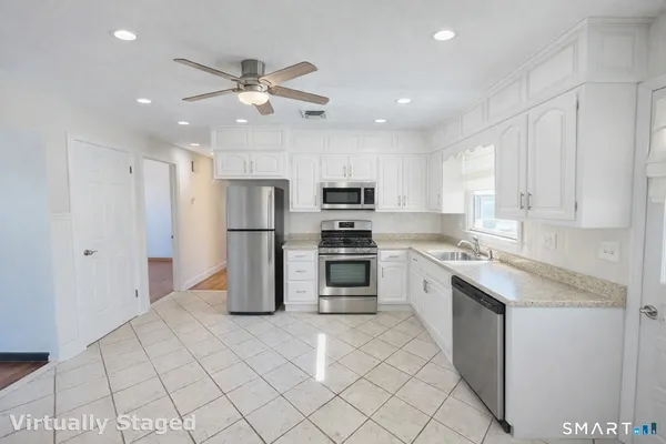 a kitchen with granite countertop a refrigerator oven a sink island and white cabinets