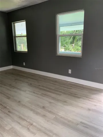 a view of an empty room with wooden floor and a window