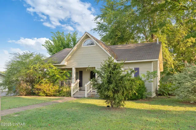 a view of a house with a yard plants and large tree