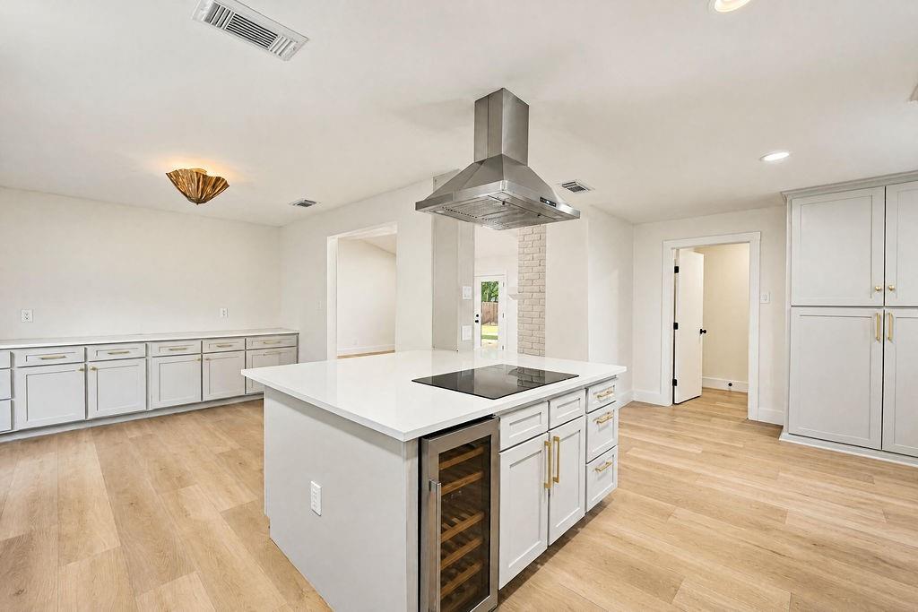 1904 Apollo Road Richardson, TX 75081 - Photo 12 of 40 Kitchen featuring an expansive center island with an integrated cooktop and under-counter wine cooler, light wood-finish flooring, recessed lighting, and extensive white cabinetry with gold-finish hardware