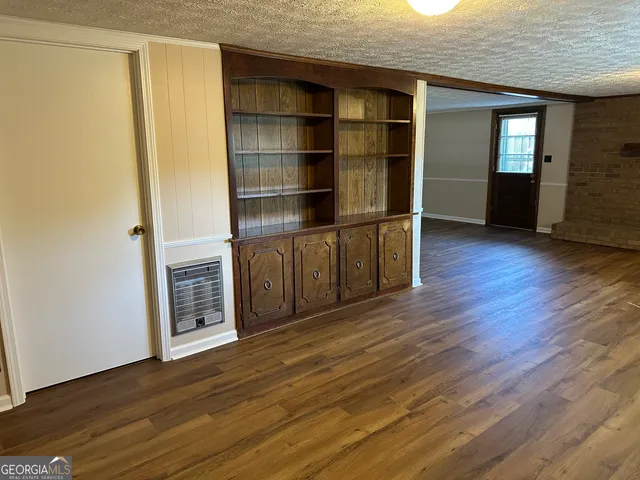 a view of empty room with wooden floor and kitchen