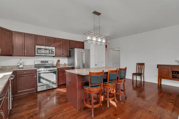 a kitchen with stainless steel appliances granite countertop a stove top oven a sink dishwasher a dining table and chairs with wooden floor