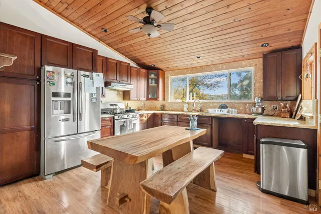 a kitchen with stainless steel appliances granite countertop a refrigerator a sink dishwasher a stove and white countertops with wooden floor