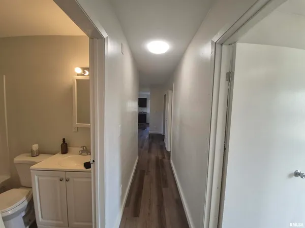 a view of a hallway with wooden floor and a bathroom