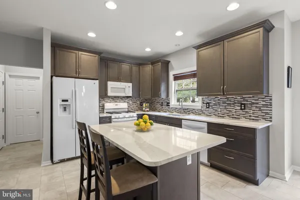 a kitchen with stainless steel appliances kitchen island granite countertop a dining table chairs and a refrigerator