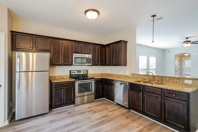 a kitchen with stainless steel appliances granite countertop a stove a sink dishwasher a refrigerator and a oven with wooden floor