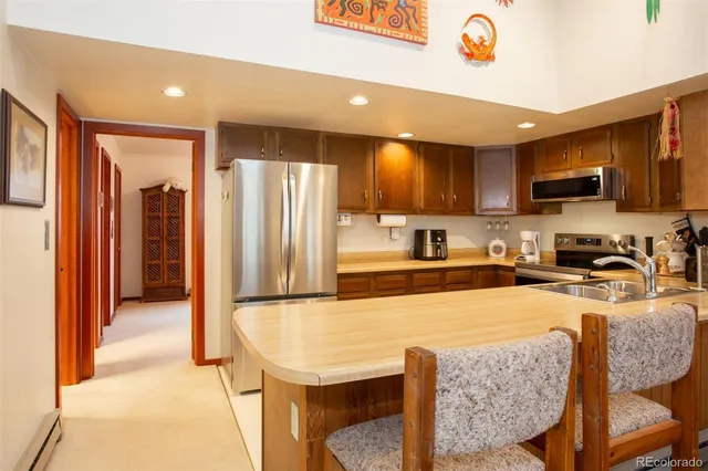 a kitchen with stainless steel appliances granite countertop a refrigerator a stove a sink a dining table and chairs with wooden floor