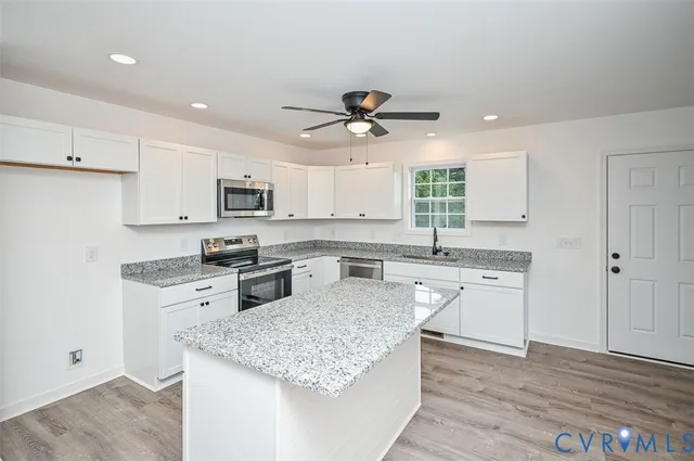 a kitchen with stainless steel appliances granite countertop a sink dishwasher a refrigerator and white cabinets with wooden floor