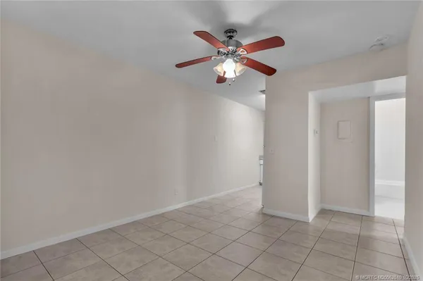 an empty room with chandelier fan and kitchen view