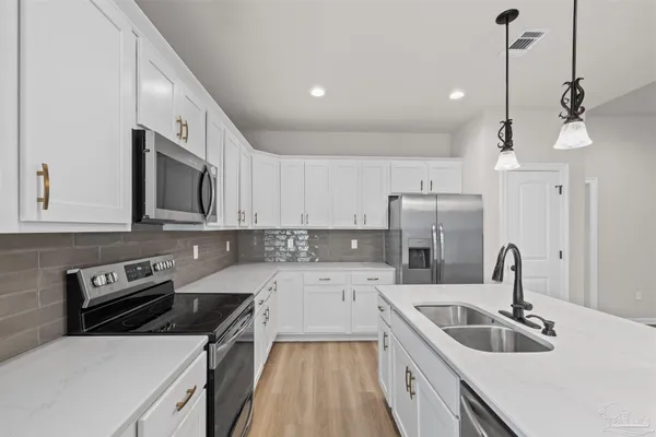 a kitchen with stainless steel appliances a stove a sink and white cabinets with wooden floor