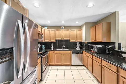 a kitchen with granite countertop stainless steel appliances a sink stove refrigerator and cabinets