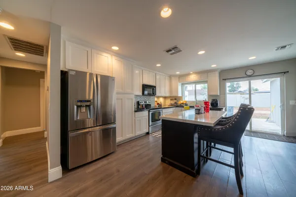 a kitchen with stainless steel appliances granite countertop a refrigerator a sink dishwasher a dining table and chairs with wooden floor