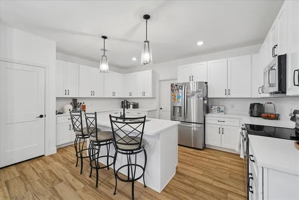 a kitchen with refrigerator a stove and white cabinets with wooden floor