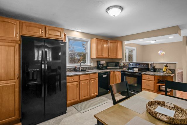 a kitchen with stainless steel appliances granite countertop a refrigerator a stove a sink and a dining table with white cabinets