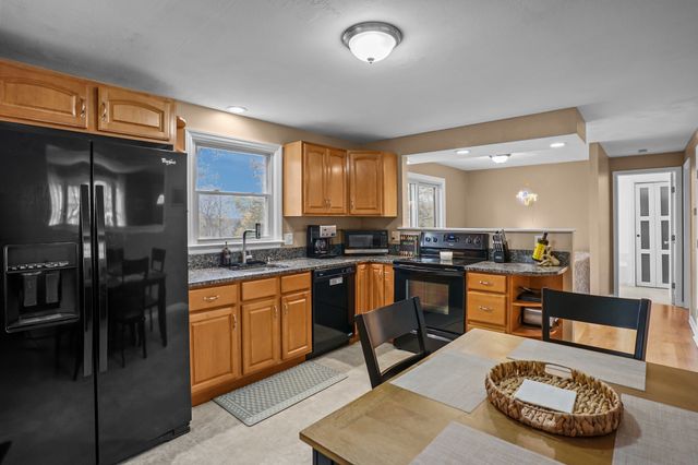 a kitchen with stainless steel appliances granite countertop a refrigerator a stove a sink a dining table and chairs with wooden floor