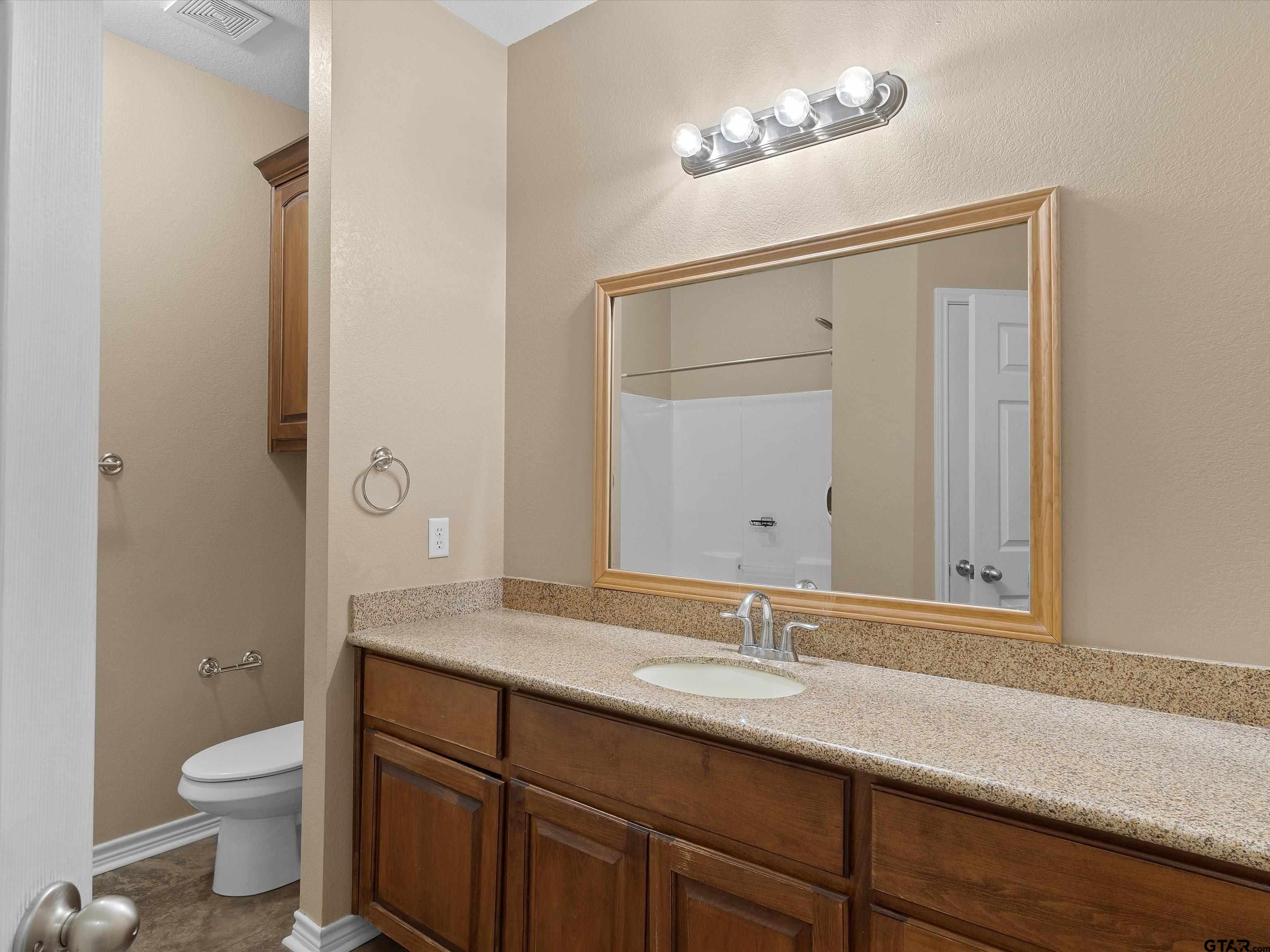 1703 Azalea Street Gilmer, TX 75644 - Photo 27 of 34 a bathroom with a granite countertop sink a toilet and a mirror
