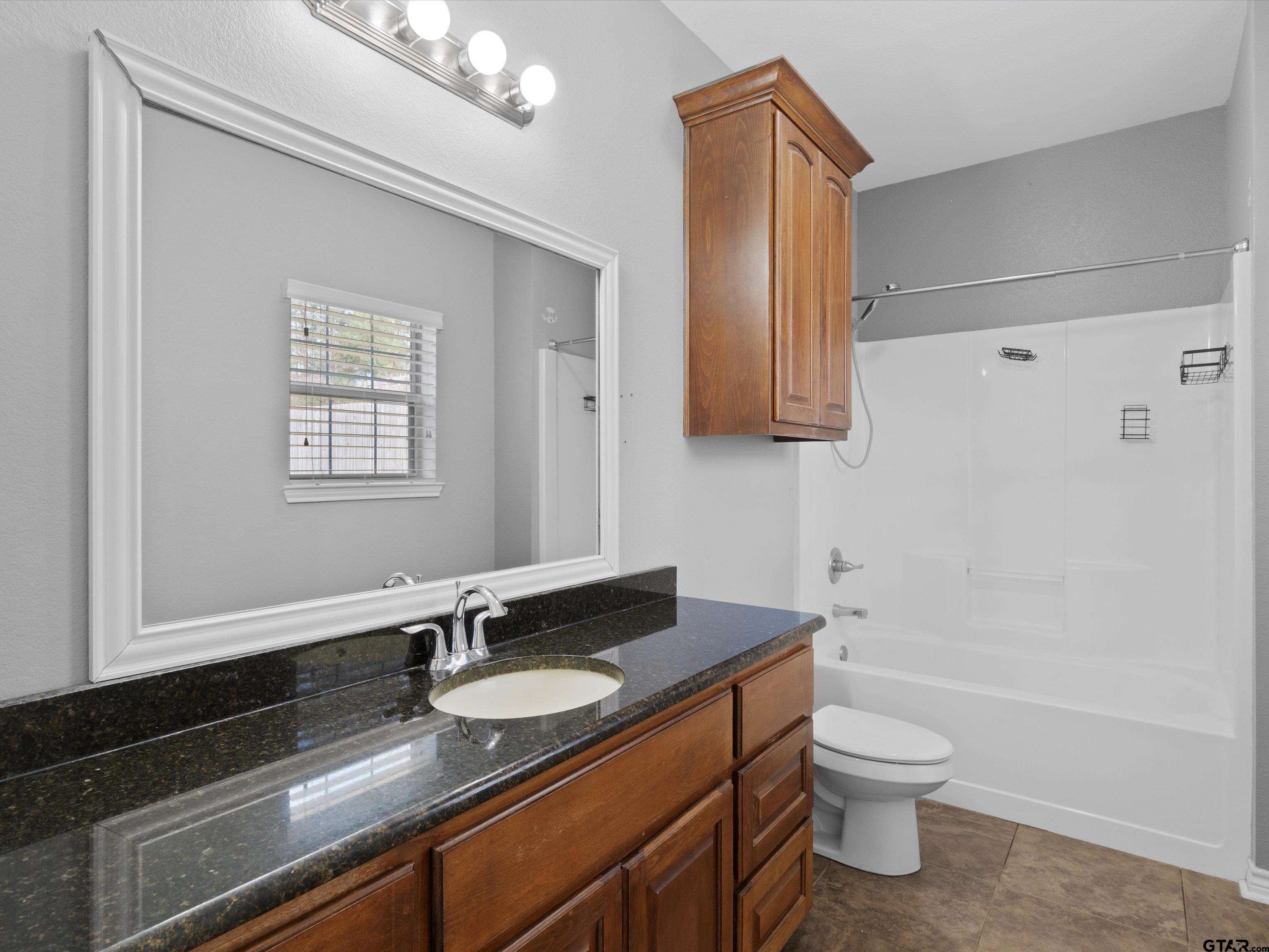 1703 Azalea Street Gilmer, TX 75644 - Photo 29 of 34 a bathroom with a granite countertop sink a toilet and bathtub