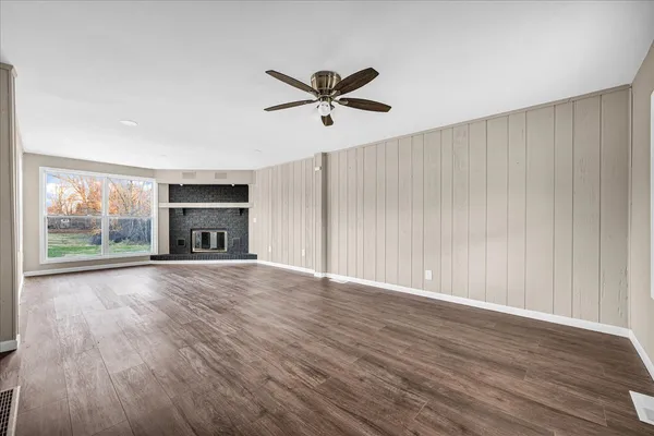 an empty room with wooden floor a ceiling fan a fireplace and windows