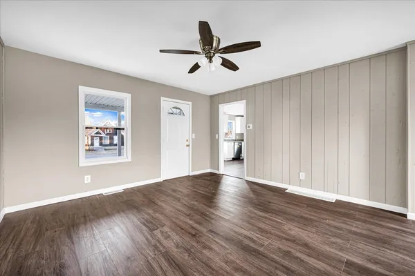 an empty room with wooden floor ceiling fan and windows