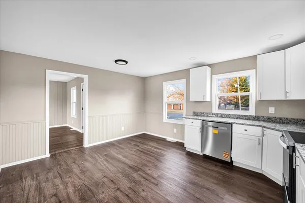 a kitchen with granite countertop a stove a sink and white cabinets with wooden floor next to windows