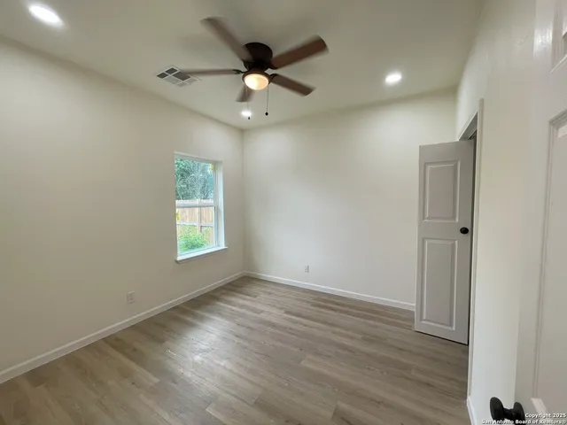 an empty room with wooden floor fan and windows