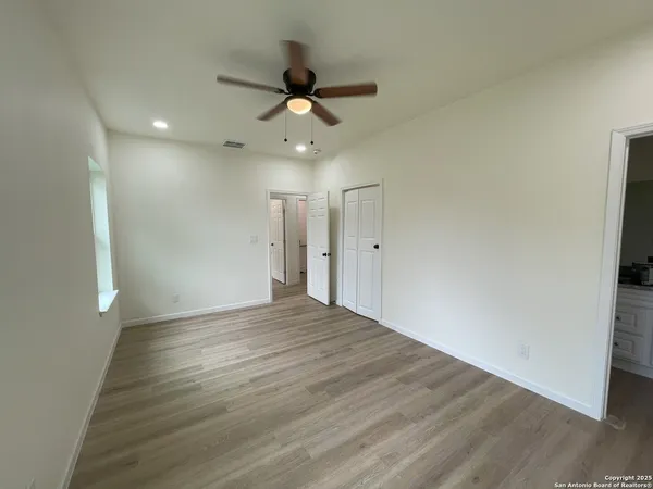 a view of an empty room with wooden floor and a ceiling fan