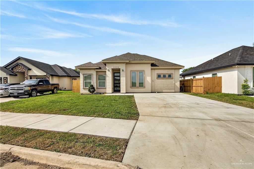 1920 Trinity Street Donna, TX 78537 - Photo 3 of 23 Contemporary stucco exterior featuring a dark asphalt shingle roof, a prominent front entry with a dark-framed glass door, and an attached two-car garage