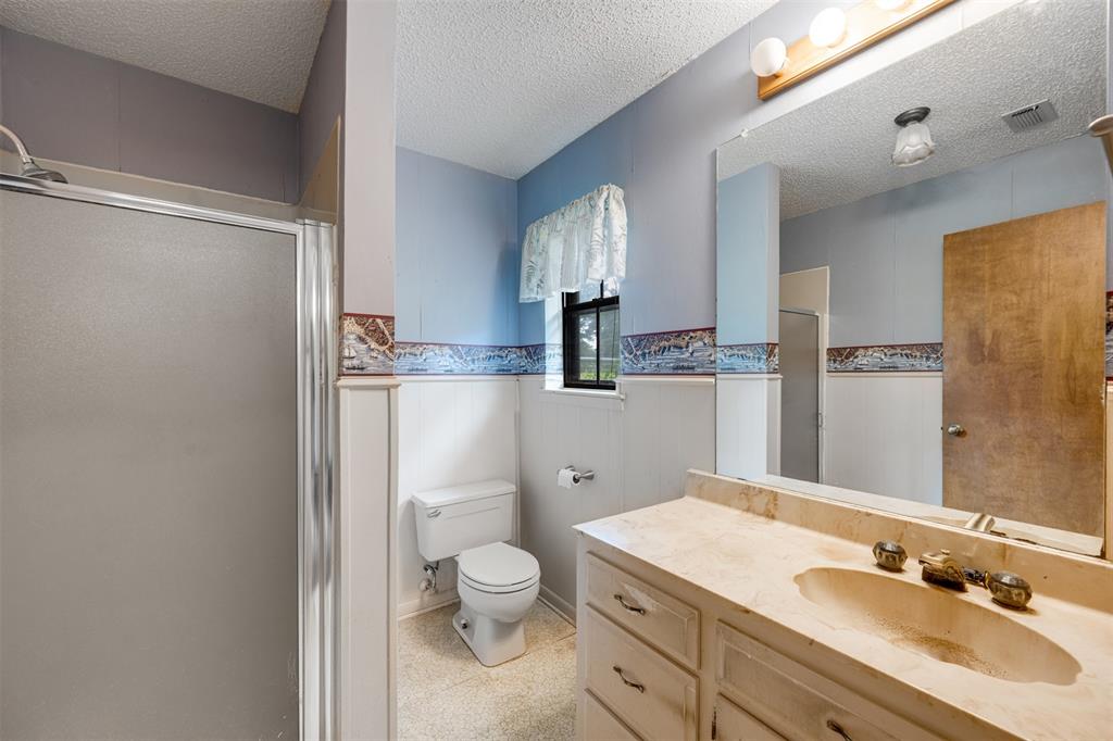 8798 Hill N Dale Road Tyler, TX 75709 - Photo 18 of 31 Bathroom featuring a shower with a frosted glass enclosure, a vanity with an integrated sink and light-colored countertop, and a built-in toilet