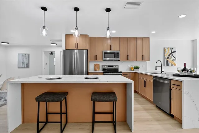 a kitchen with stainless steel appliances a sink a stove a refrigerator and chairs