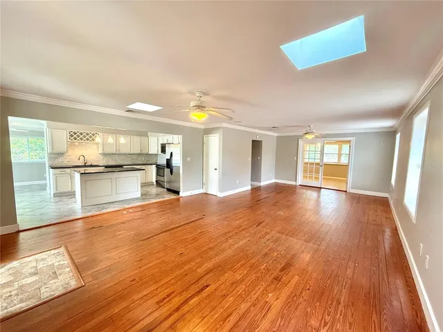 a view of empty room with wooden floor and kitchen view