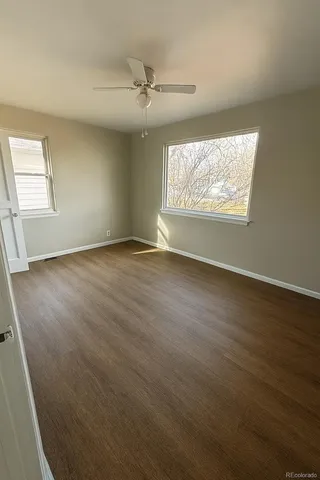 an empty room with wooden floor fan and windows