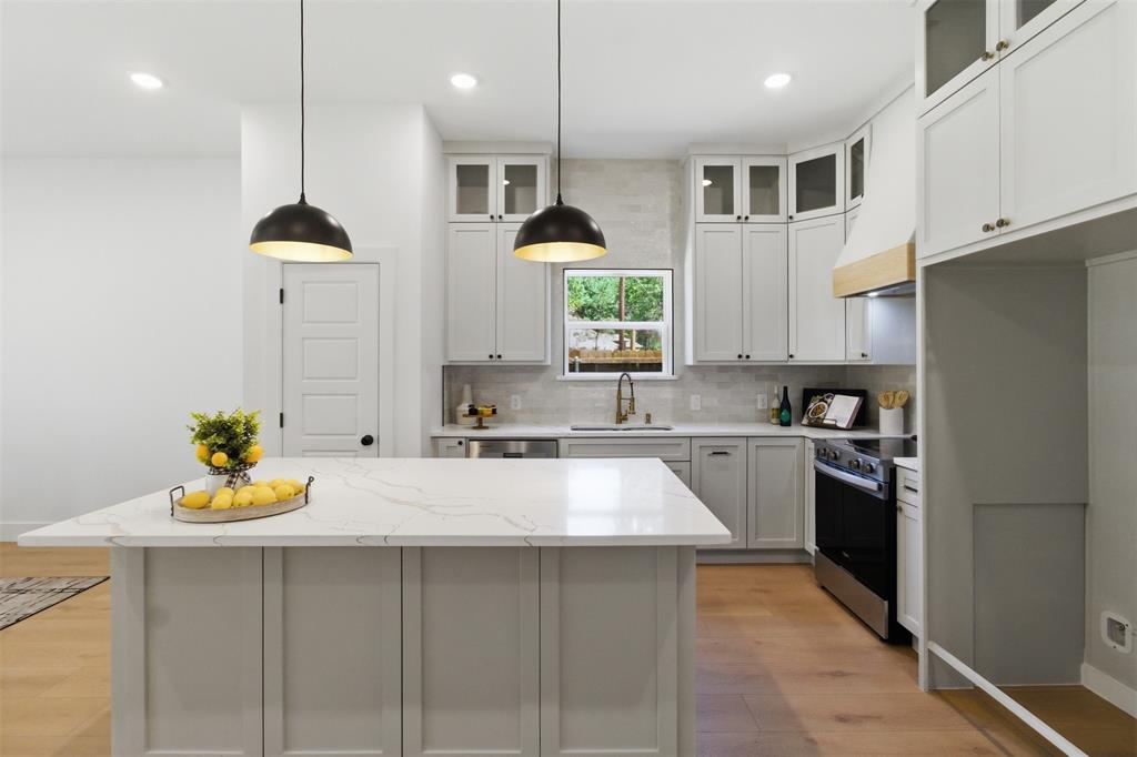 435 Waterboard Road Trinidad, TX 75163 - Photo 12 of 39 Kitchen featuring a substantial island with a light-toned countertop, white cabinetry with glass upper doors, wood-finish flooring, a stainless steel range, and two pendant light fixtures