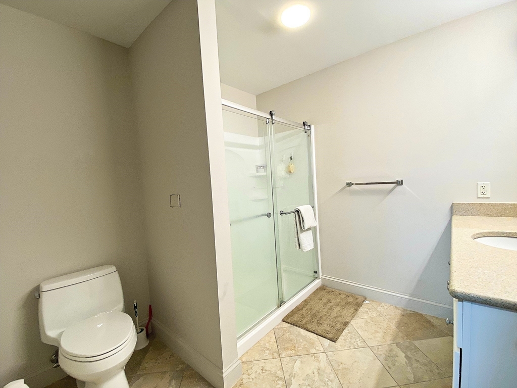 318 Rindge Avenue, Unit 405 Cambridge, MA 02140 - Photo 17 of 25 a bathroom with a granite countertop toilet and a shower