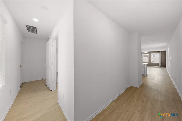 a view of a hallway with wooden floor and a bathroom
