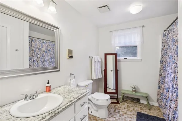 a bathroom with a granite countertop sink toilet a mirror and shower curtain