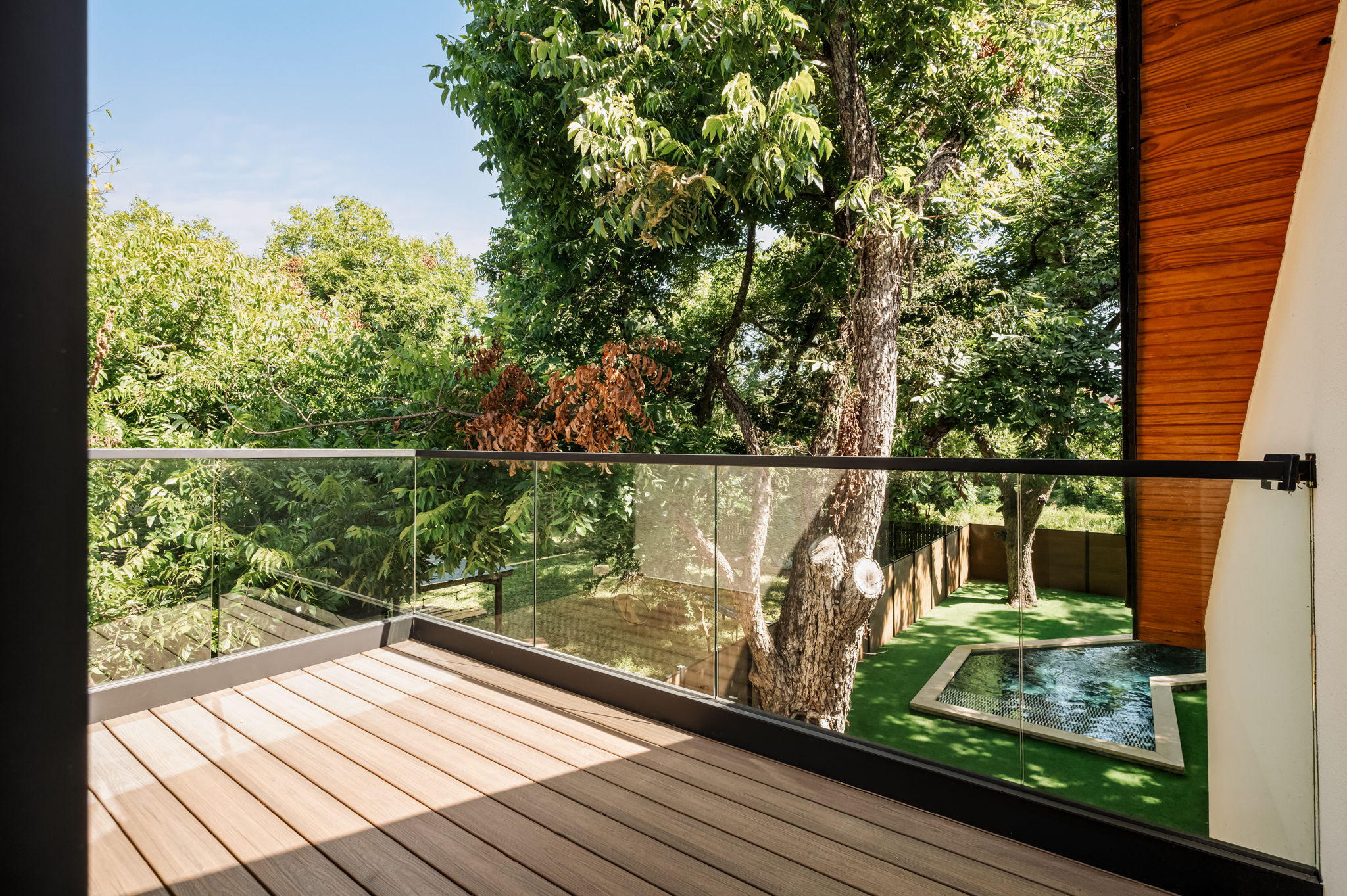 3210 Thompson Street Austin, TX 78702 - Photo 22 of 39 A private balcony with wood flooring overlooks a lush yard and tranquil pool, offering a serene outdoor escape.