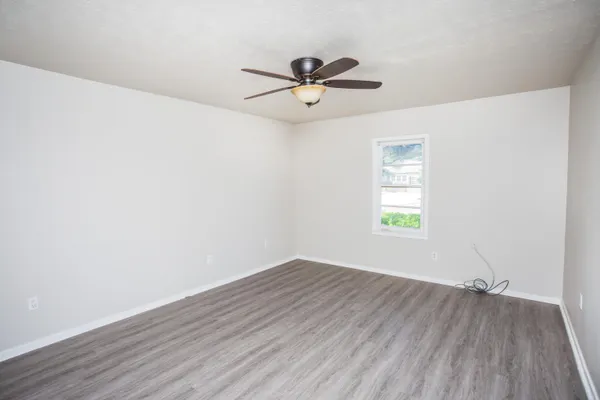 an empty room with wooden floor ceiling fan and windows