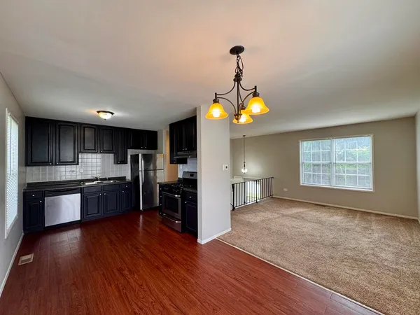 a kitchen with stainless steel appliances granite countertop a stove a refrigerator wooden floor and a view of living room