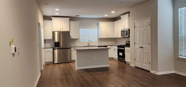 a kitchen with stainless steel appliances granite countertop a refrigerator a sink a stove and white cabinets with wooden floor